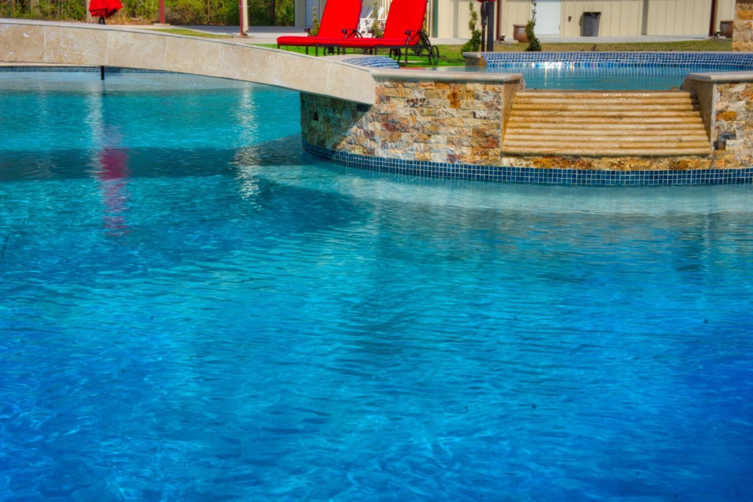 A pool with a red chair and a stone wall.