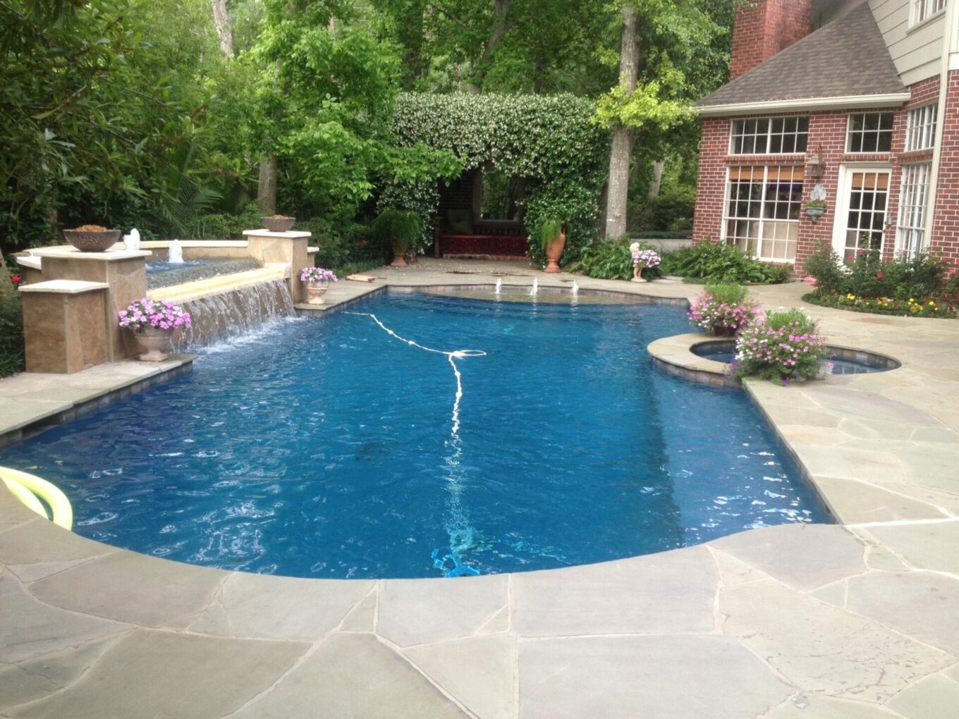 A pool with a fountain and a brick wall.
