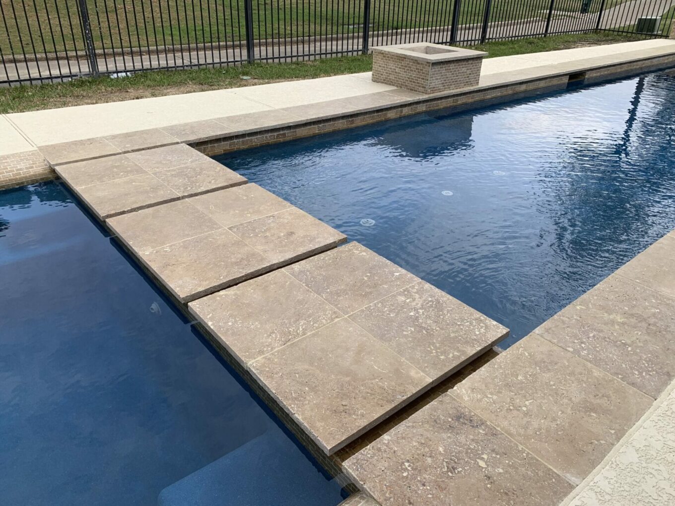 A pool with a stone deck and water features.