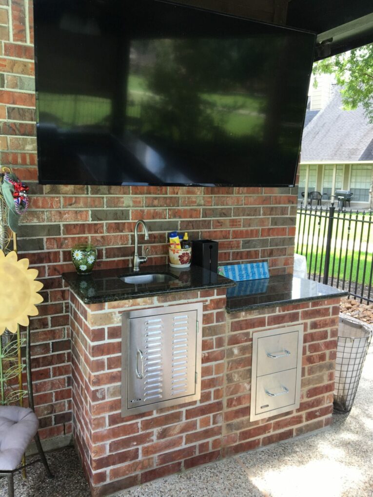 A television mounted on the wall above an outdoor kitchen.
