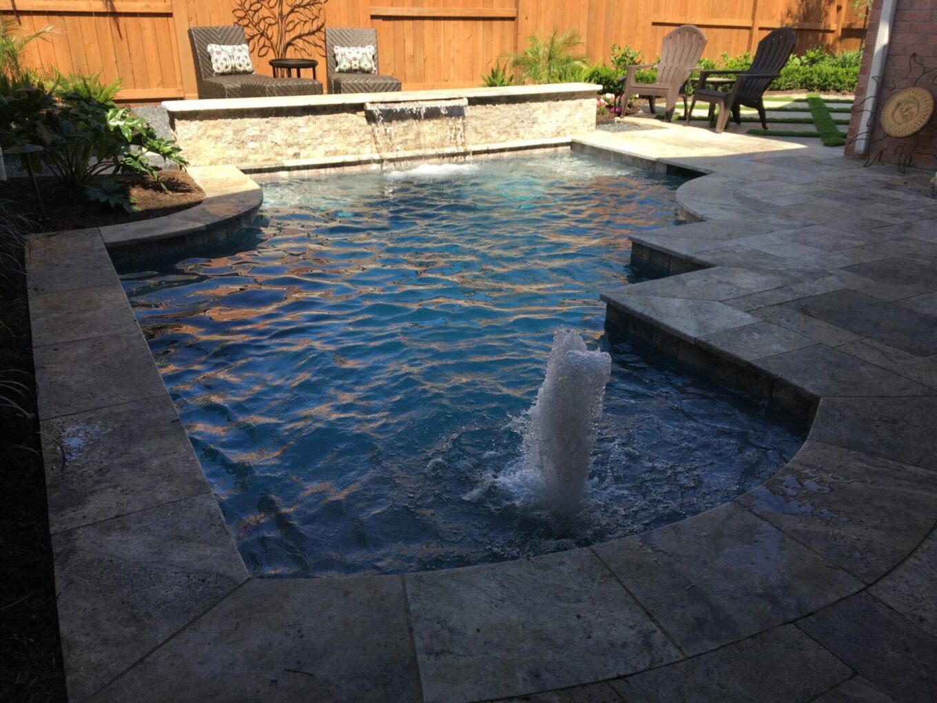 A pool with a fountain and steps in the back yard.