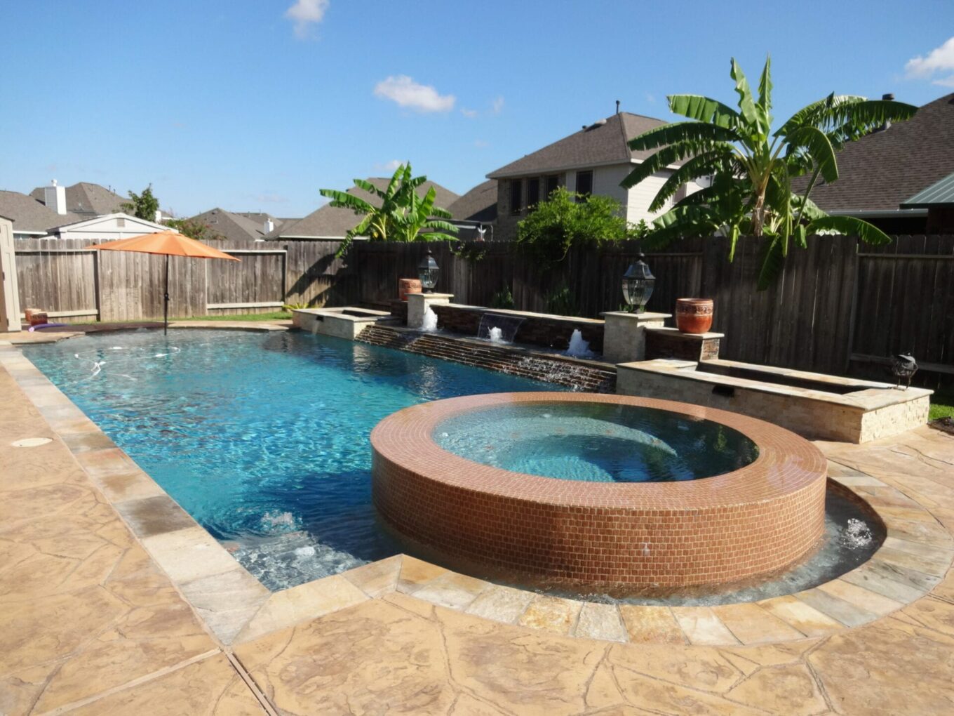 A pool with a jacuzzi and a large stone wall.