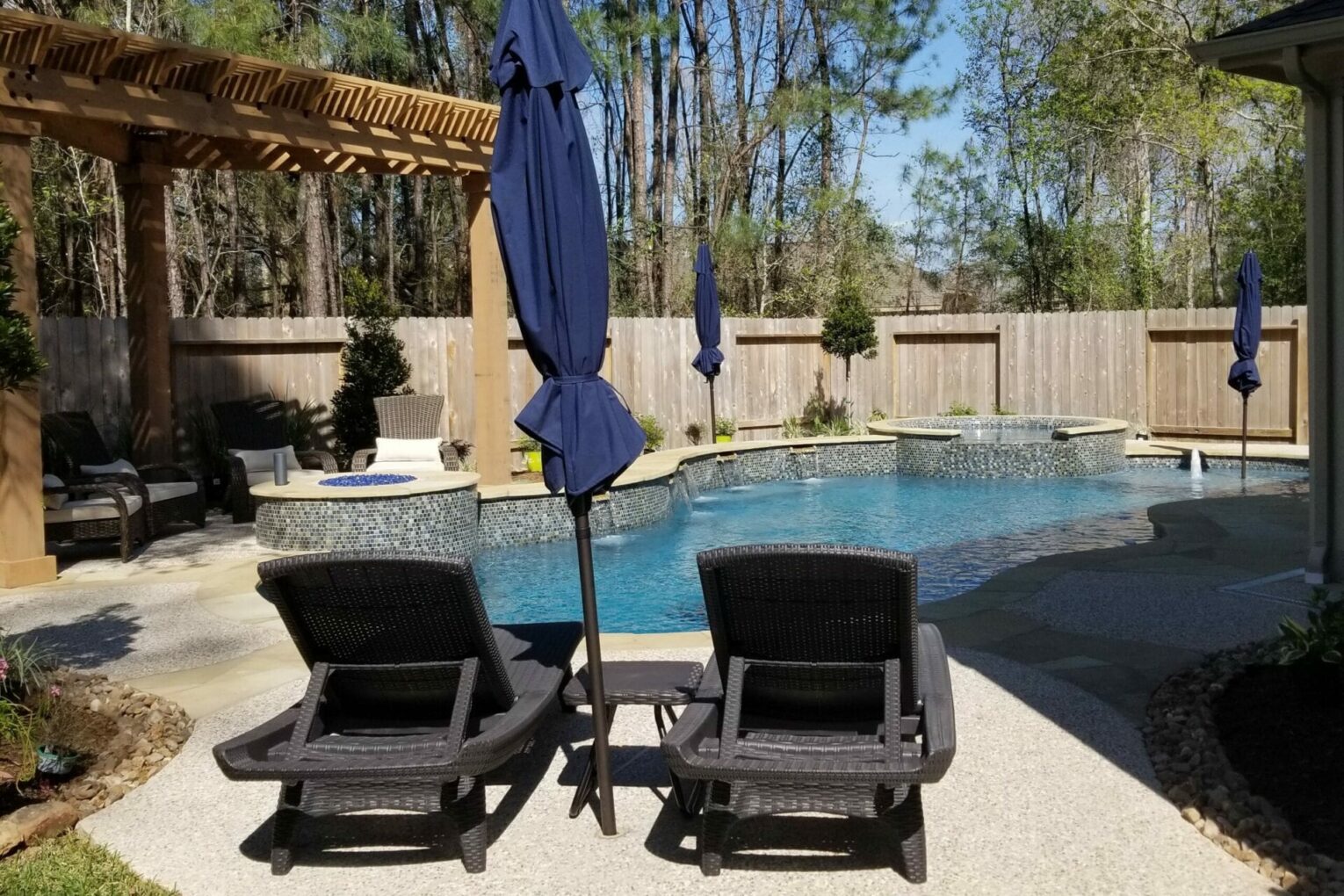 Two lounge chairs and a table in front of the pool.