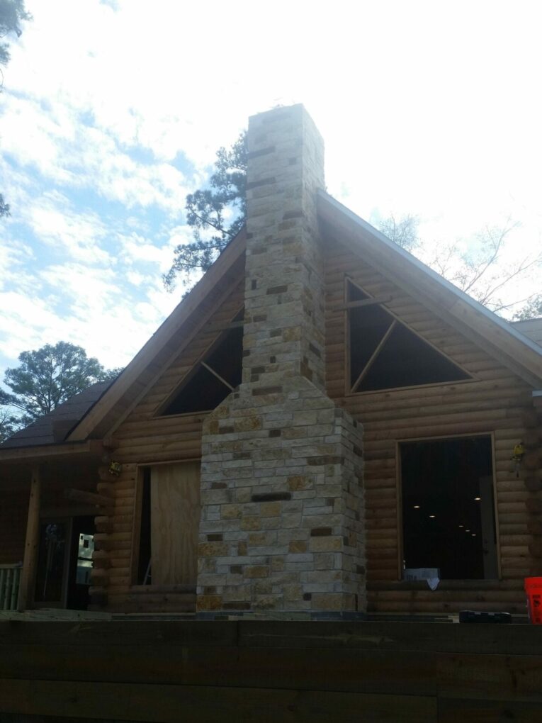 A log cabin with a stone chimney in the middle of it.